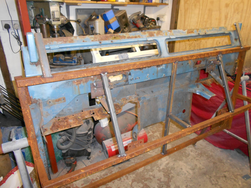 Old rusty Land Rover Series 3 bulkhead in a jig ready to be repaired viewed from the front.